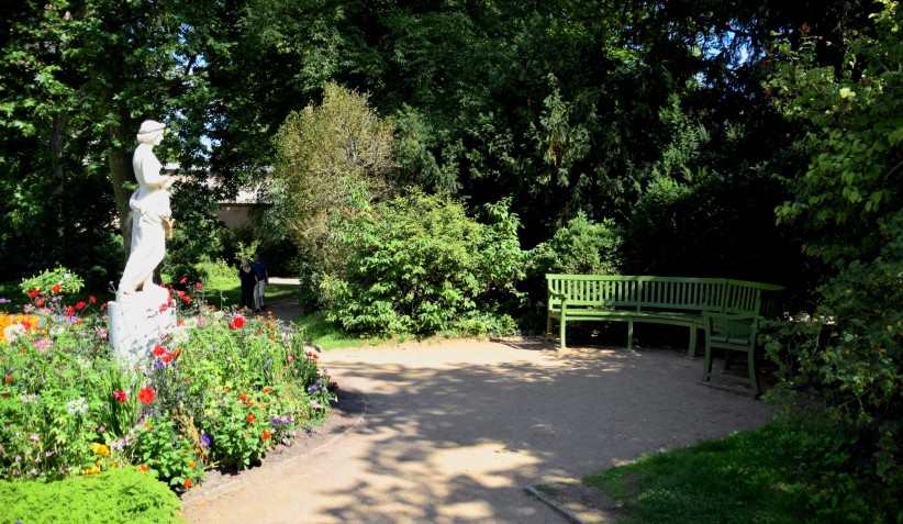 Teeplatz - halbrunde Sitzbank vor Florastatue im Gebsch.